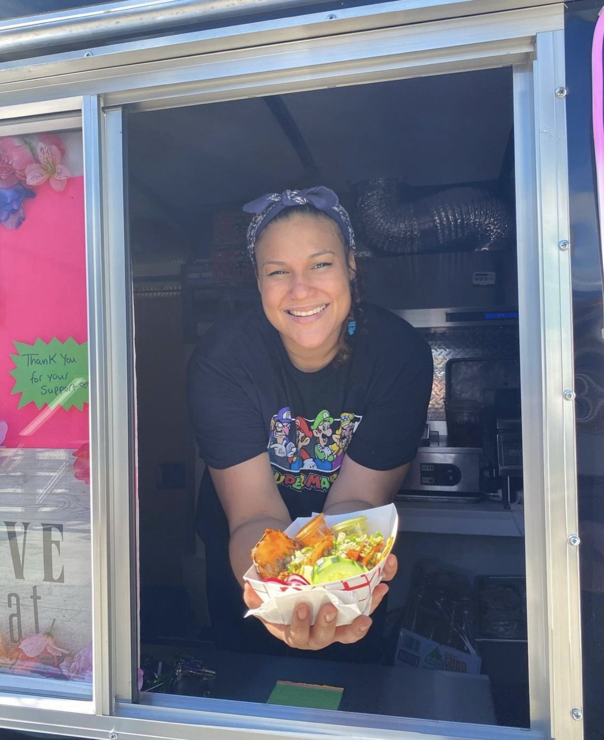 Chef Nadine Moore smiling in the truck window holding a tray of food