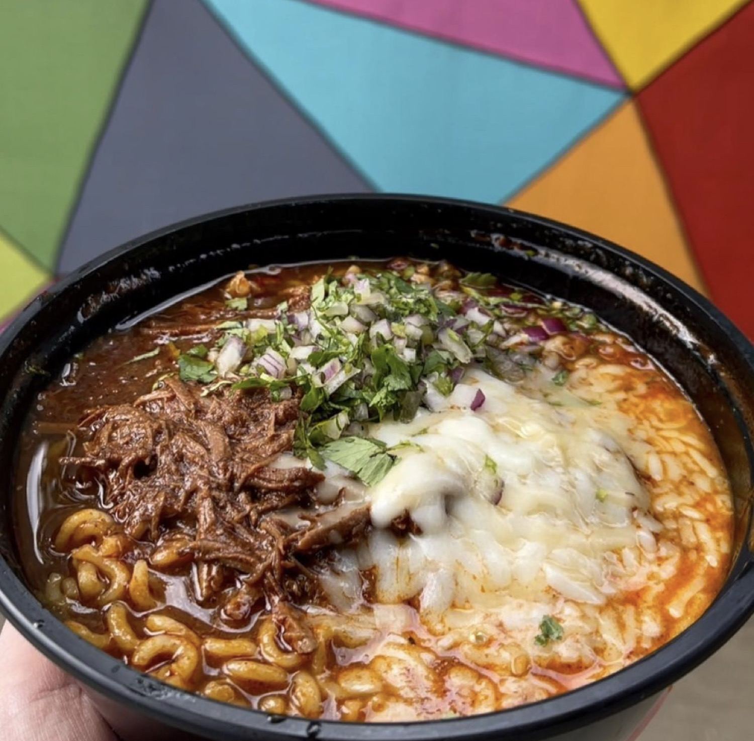 A bowl of birria with melted cheese and cilantro